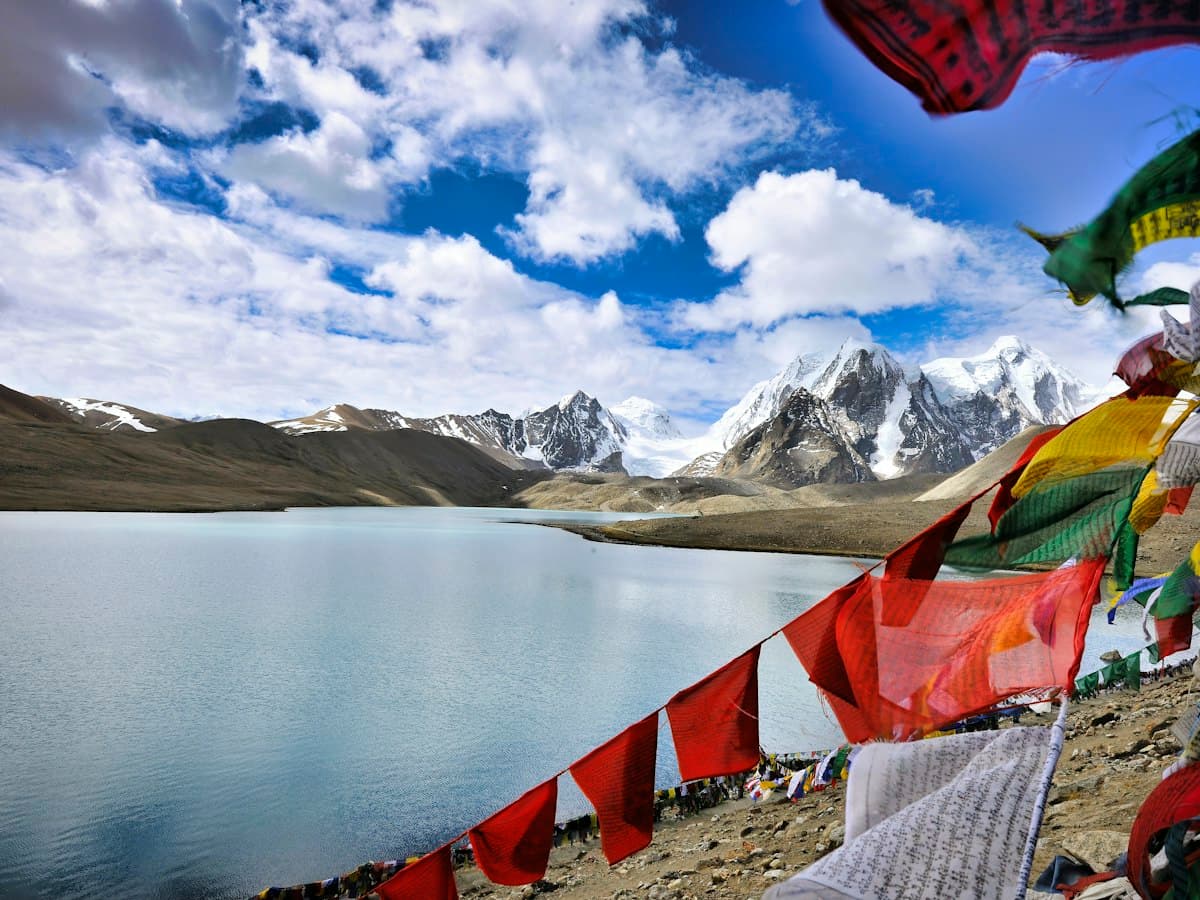 Prayer flags line the shore of Gurudongmar Lake in North Sikkim with snow peaks behind.