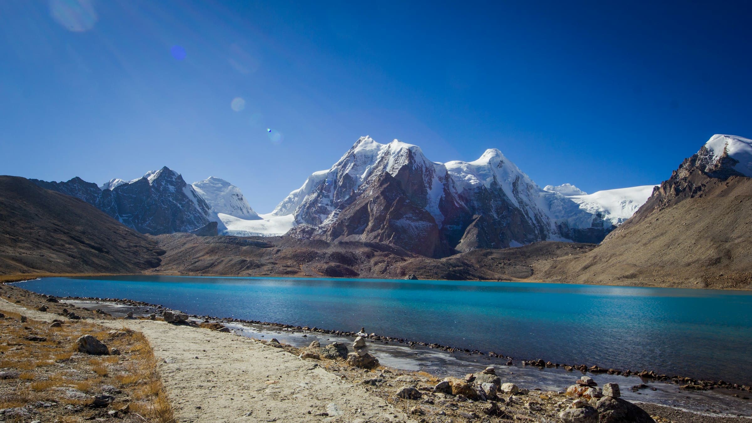 Gurudongmar Lake in North Sikkim mirroring snow-capped peaks under a clear blue sky.