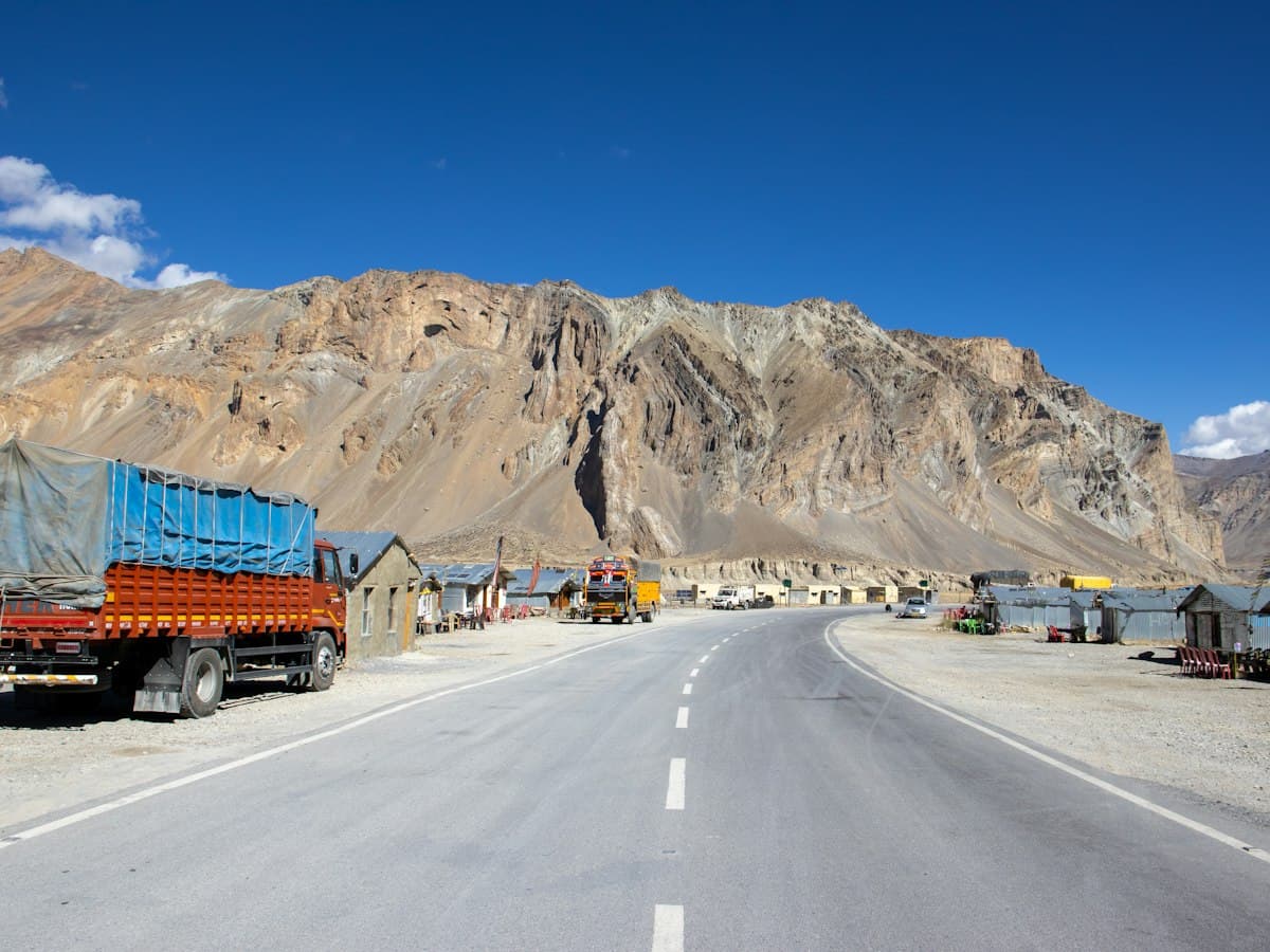 A truck drives a rough mountain road below bare high-altitude peaks in Ladakh, India.
