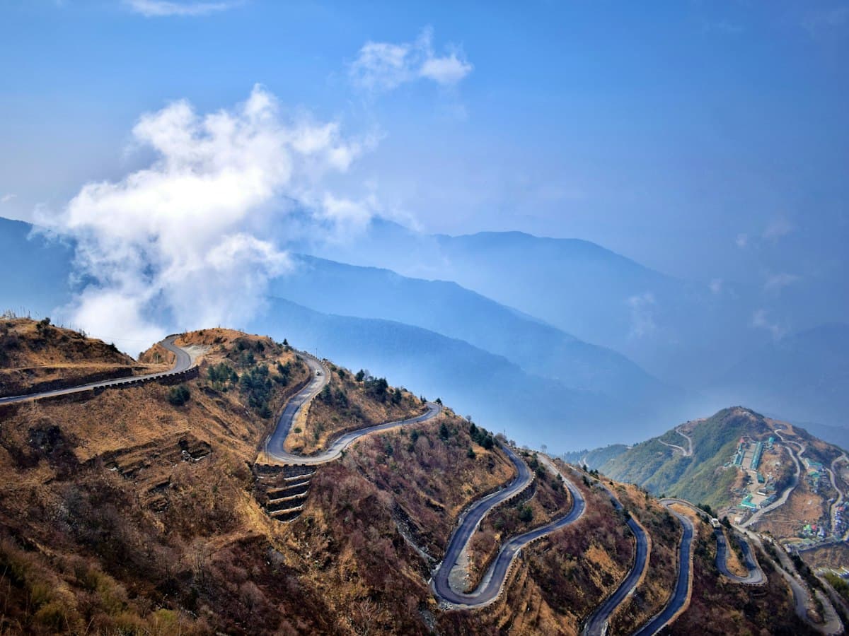 A paved road winds up green forested hills in Sikkim, northeast India.