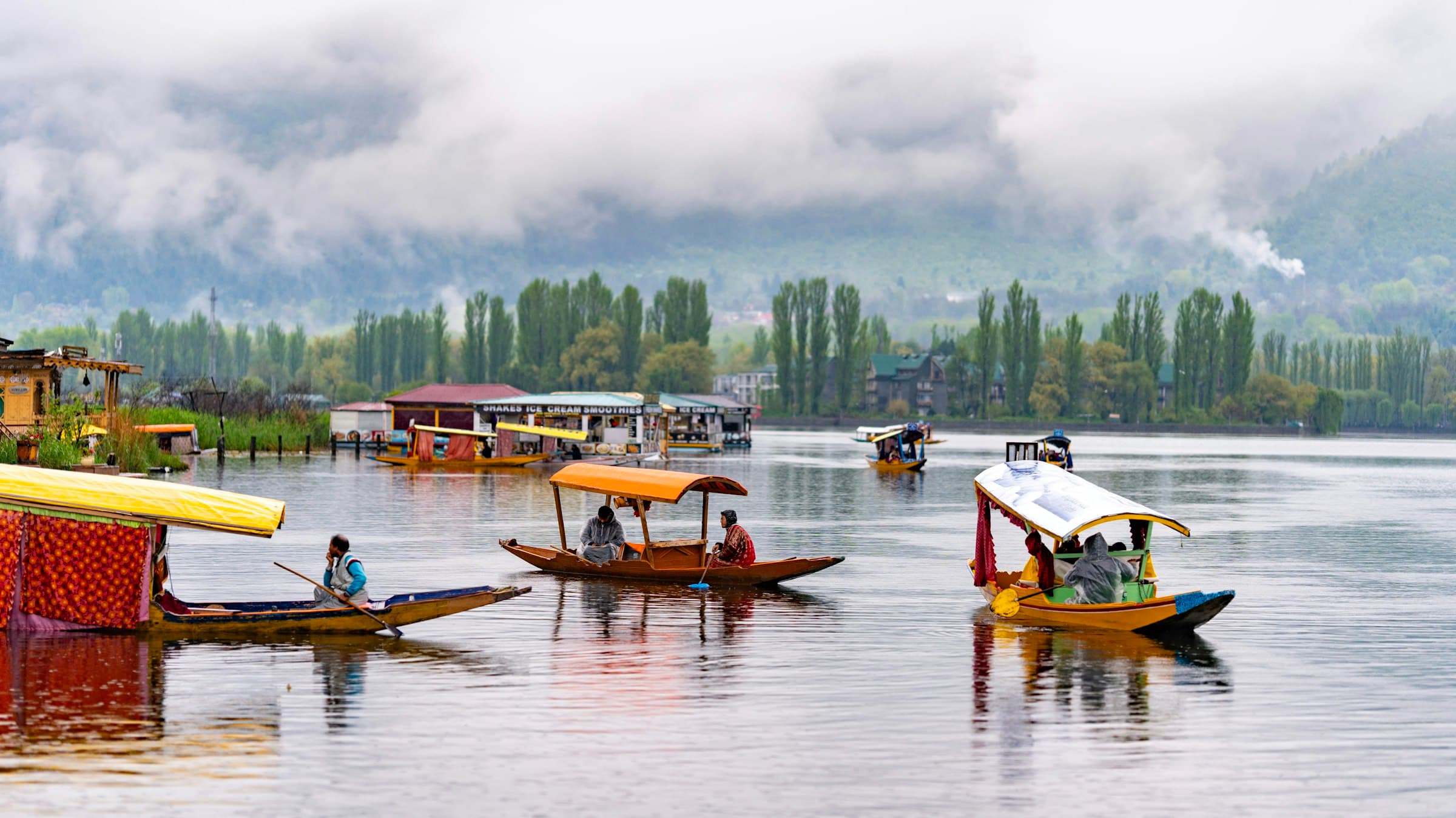 Wooden boats float on the still water of Dal Lake below hazy mountains in Srinagar, Kashmir.