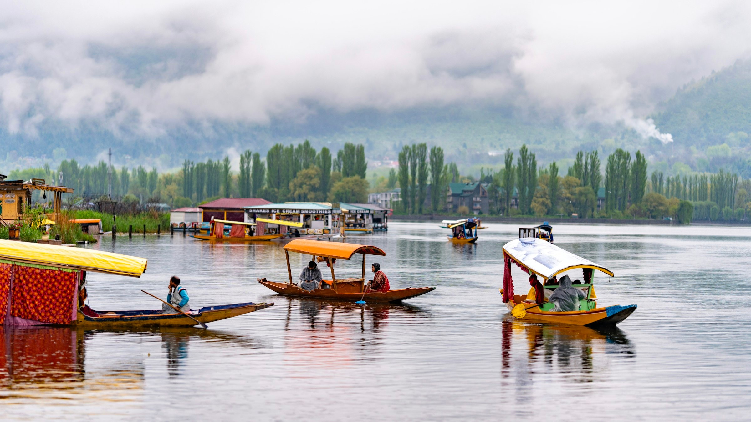 Wooden boats float on the still water of Dal Lake below hazy mountains in Srinagar, Kashmir.