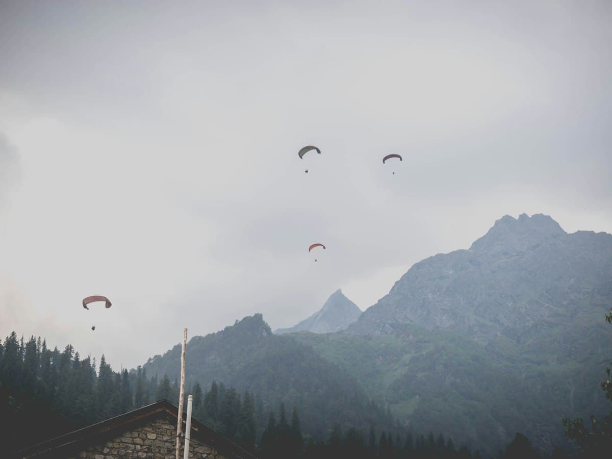 Paragliders drift above the green Solang Valley near Manali with mountains rising behind.
