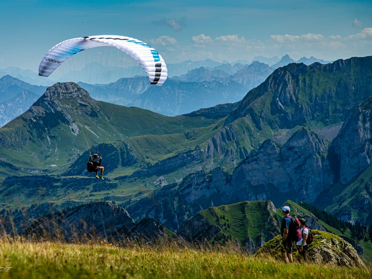 A tandem paraglider in flight over a green Himalayan valley near Solang.