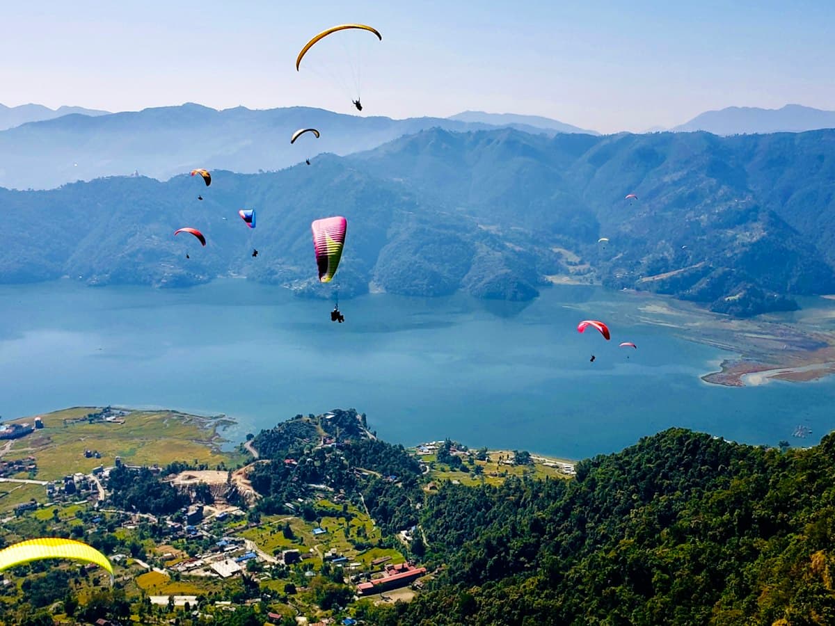 Paragliders soar high above a patchwork of green fields, as at the Bir-Billing site.