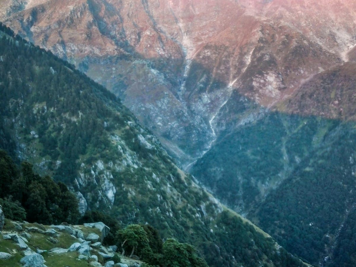 The open grassy ridgeline of Triund with brown-green slopes and higher mountains beyond.