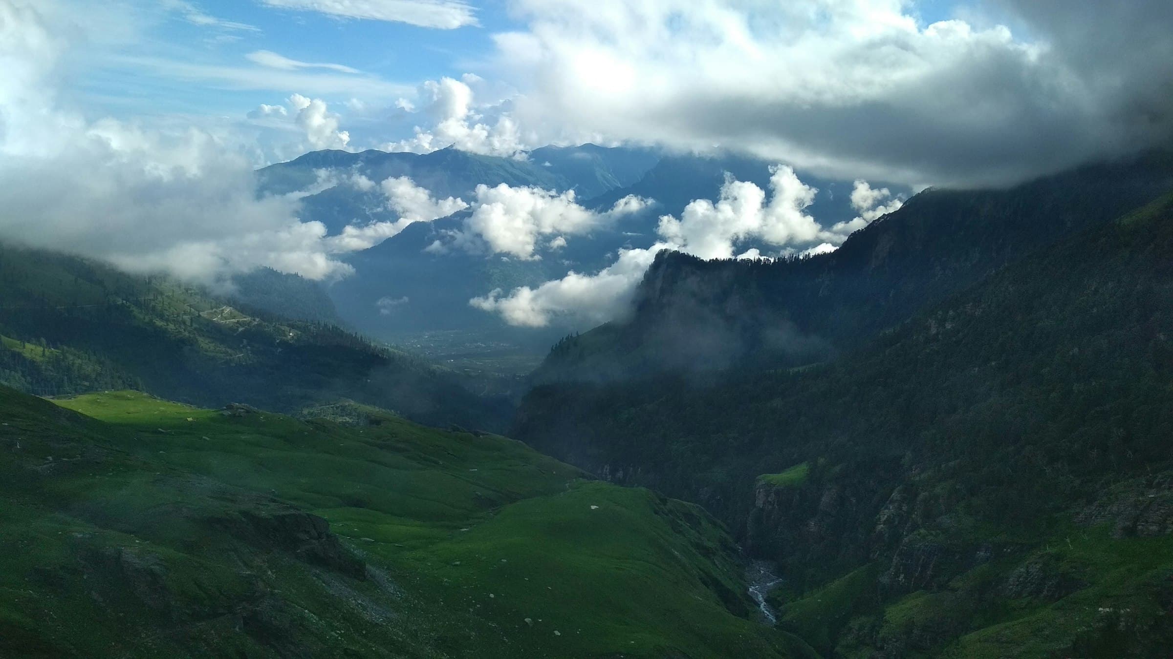 A wide green Manali valley opens toward cloud-wrapped mountains in Himachal Pradesh.