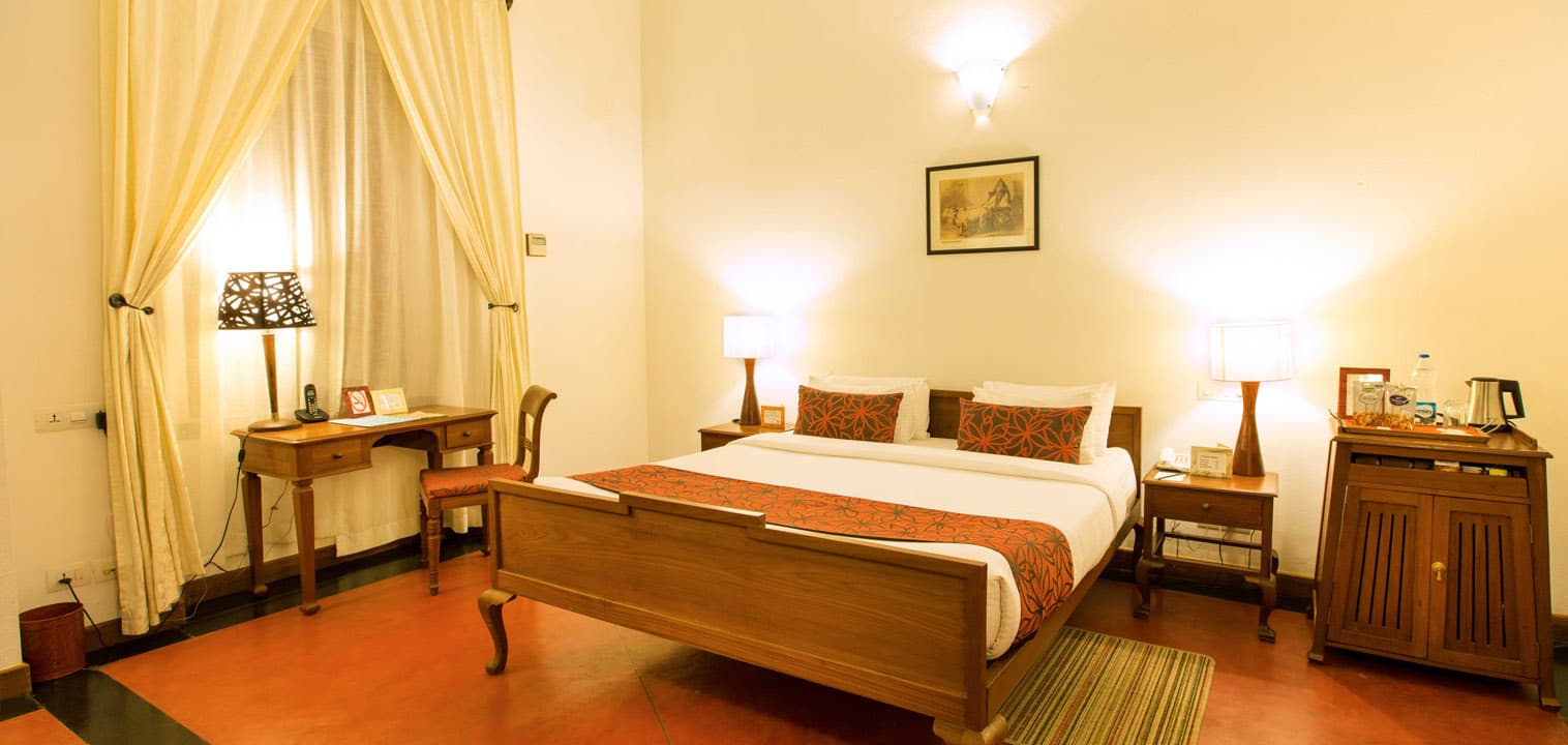 Standard room with a wooden bed and shuttered windows at Palais de Mahe, Puducherry