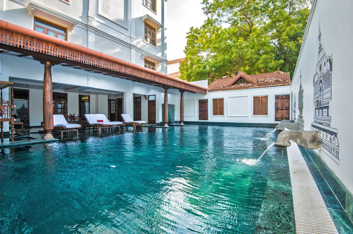 Courtyard swimming pool bordered by carved wooden colonnades at Svatma, Thanjavur, in daylight