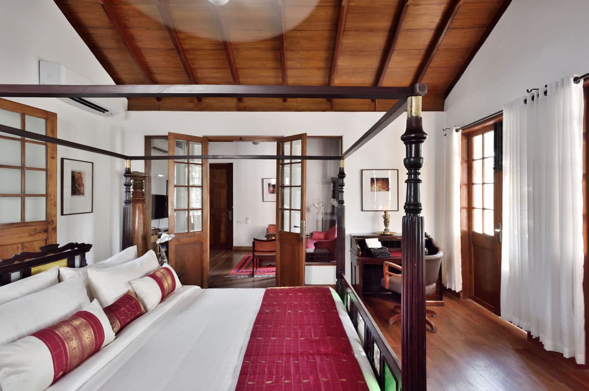 Guest room with a black four-poster bed, timber ceiling and adjoining sitting area at Svatma, Thanjavur
