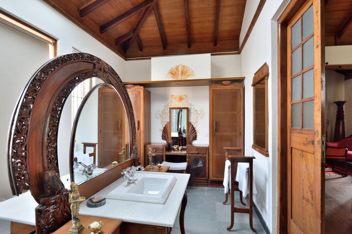 Suite dressing area with a large round carved-wood mirror and marble-topped vanity at Svatma, Thanjavur