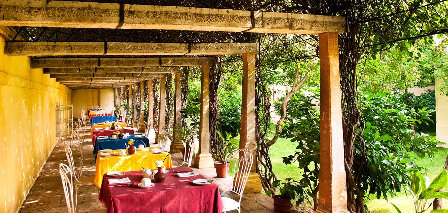 Covered garden-side dining terrace with a set table at Visalam, a CGH Earth hotel, Kanadukathan
