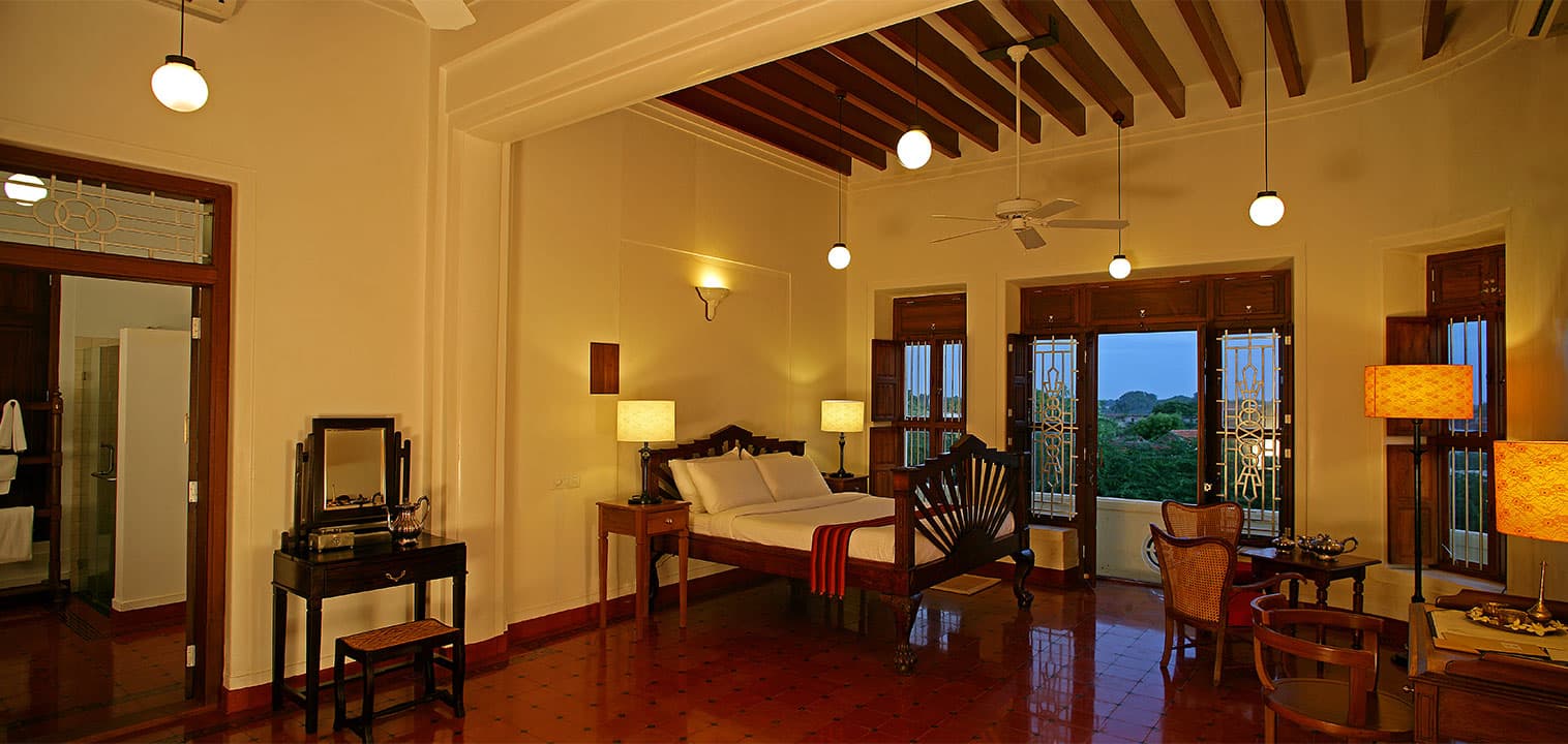 Deluxe Room with a high timber ceiling, four-poster bed and lounge chairs at Visalam, a CGH Earth hotel, Kanadukathan