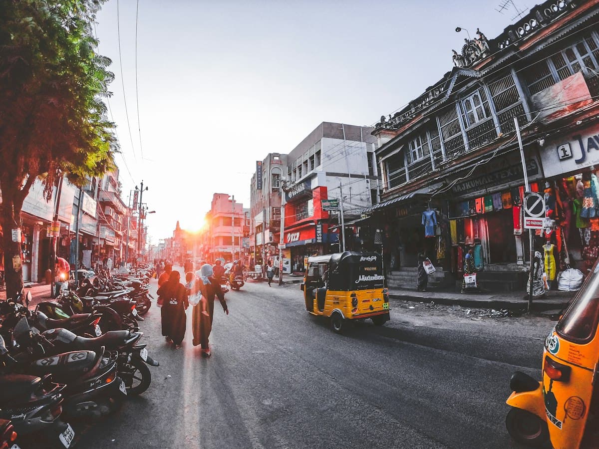 People and auto-rickshaws move through a busy bazaar street in Madurai.