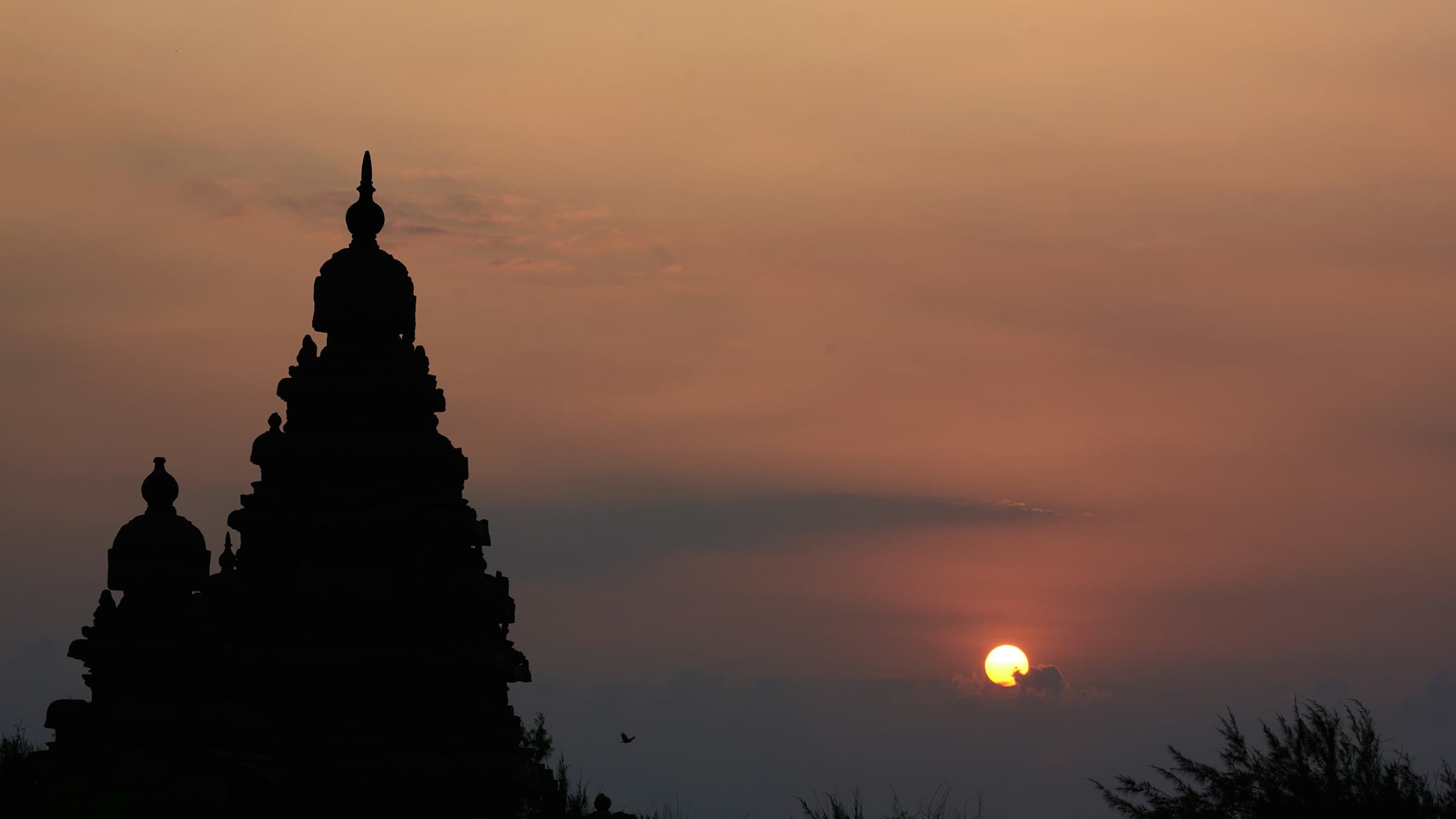 The Shore Temple at Mahabalipuram silhouetted against the sky at sunrise above the Coromandel coast.