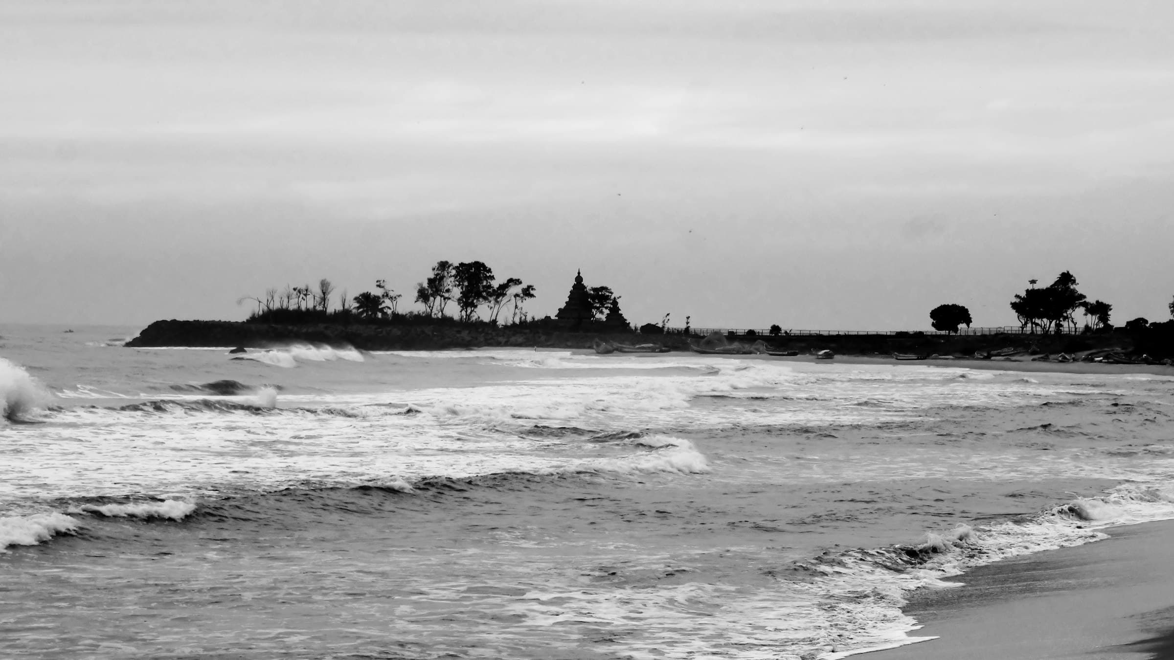 Waves roll onto a Coromandel beach with the silhouette of a Mahabalipuram temple on the horizon.