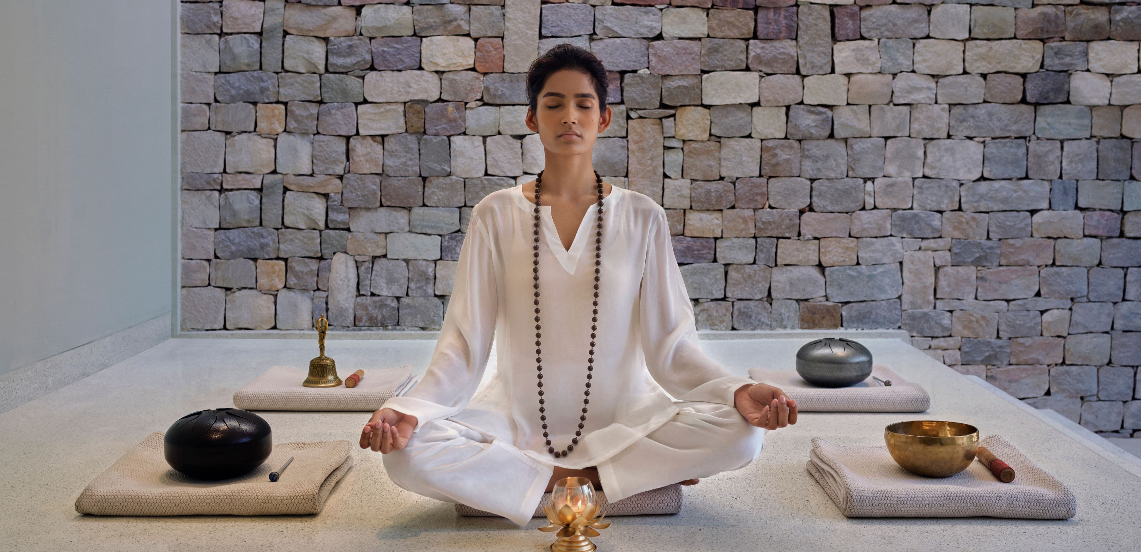 Guest in a meditation session in a stone-walled wellness room at Taj Rishikesh Resort & Spa.