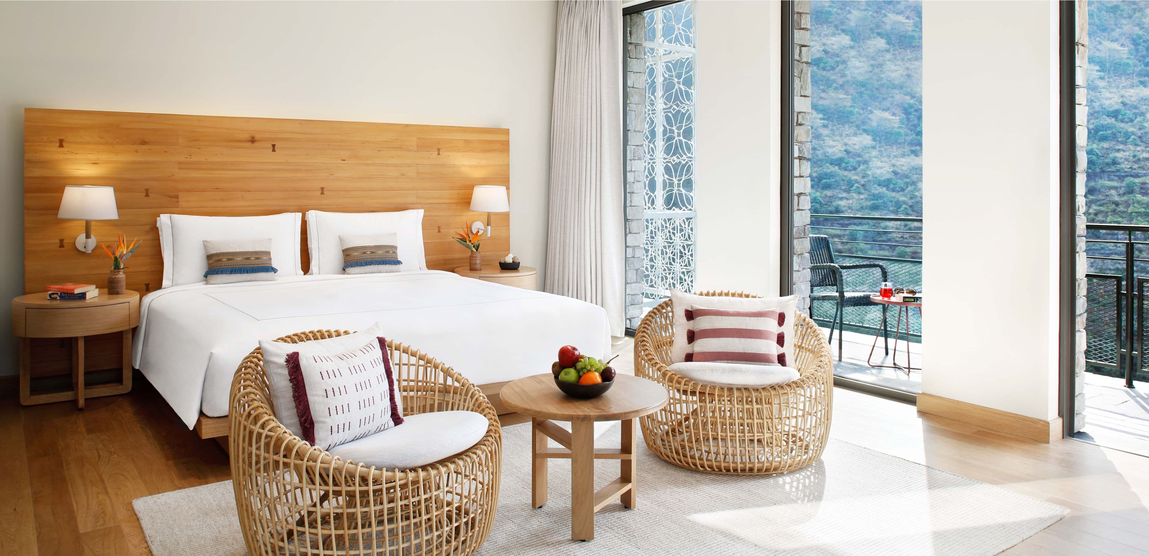Guest room bed and seating area with balcony overlooking wooded hills at Taj Rishikesh Resort & Spa.