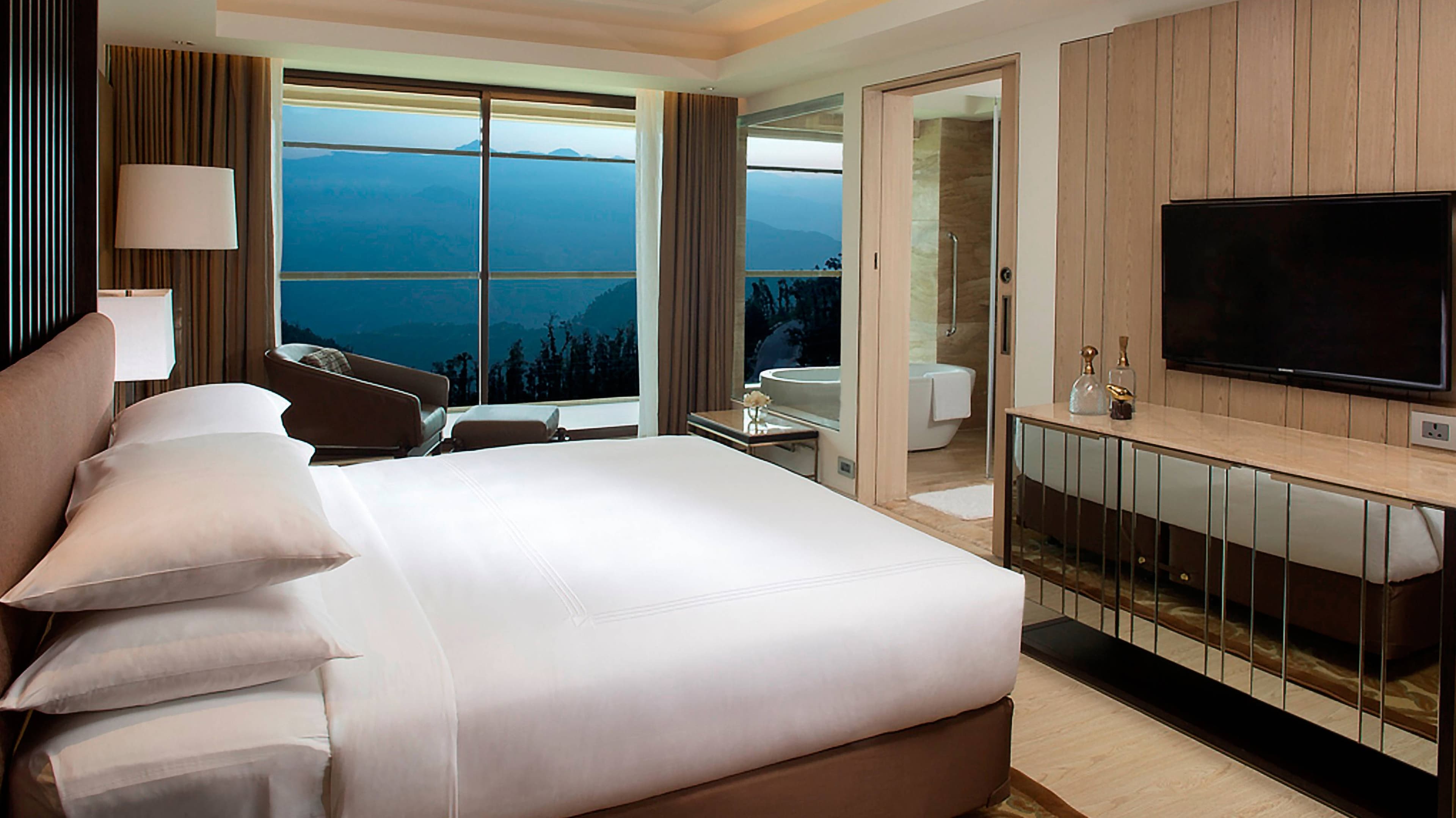 Suite bedroom with freestanding bathtub and mountain-valley view at dusk, JW Marriott Mussoorie Walnut Grove Resort & Spa.