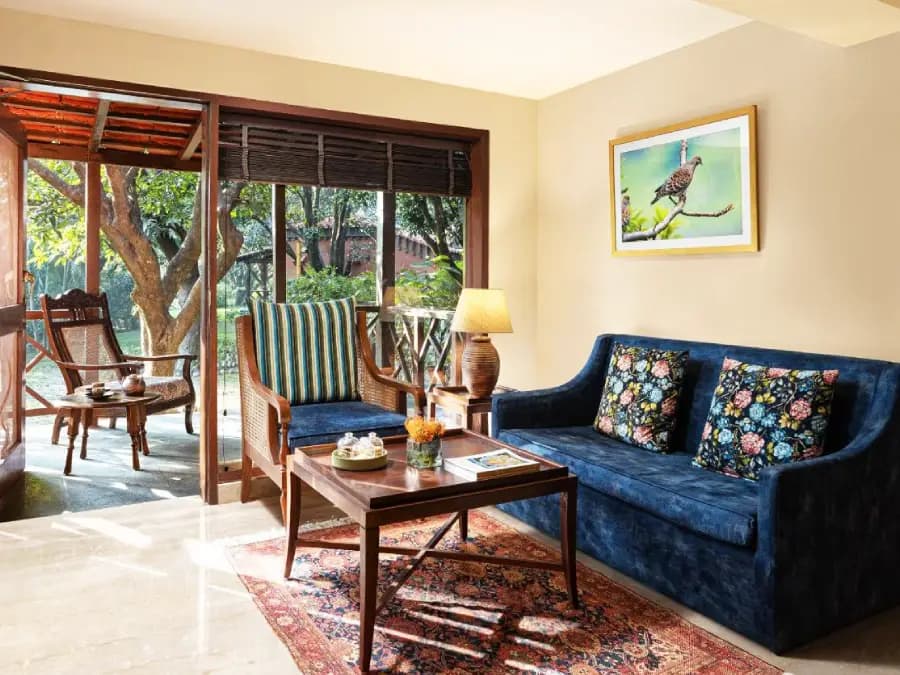 Taj Corbett Resort & Spa cottage sitting room with rattan armchairs, sliding doors to a garden, and a bird print on the wall