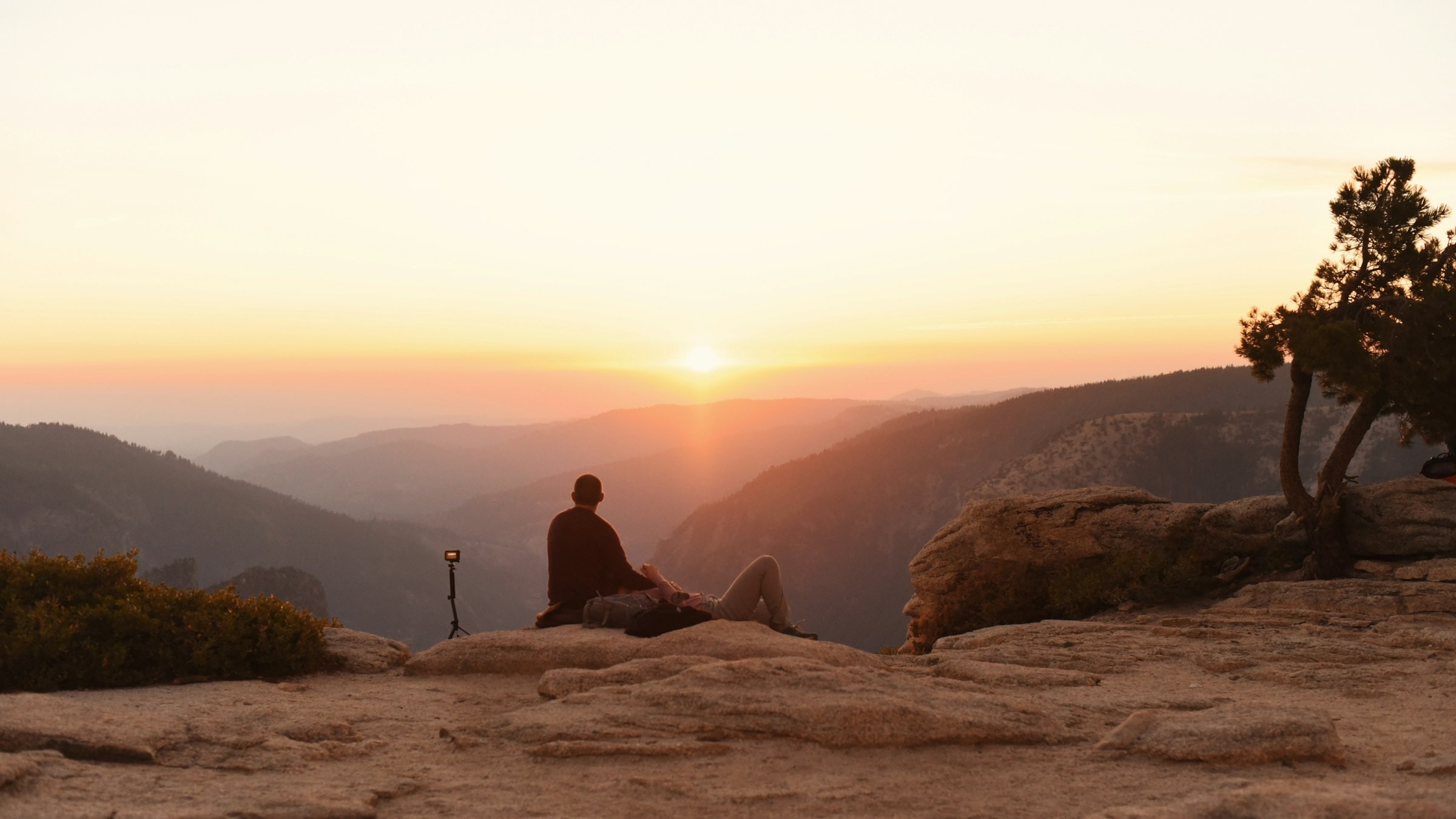 A person sits in quiet meditation on a cliff edge overlooking a mountain sunset.
