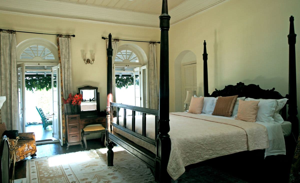 Guest suite at Glenburn Tea Estate with a dark wood four-poster bed and arched French doors opening to a private verandah