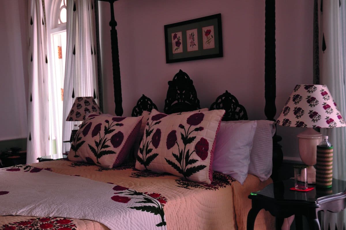 Guest suite at Glenburn Tea Estate with a carved four-poster bed dressed in pink floral linens and a botanical print above the headboard