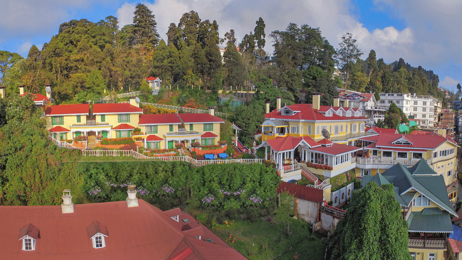 Aerial view of MAYFAIR Hill Resort Darjeeling's red-roofed colonial buildings and gardens set into the wooded hillside