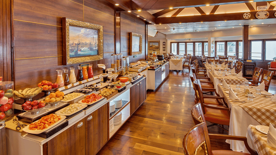 Wood-panelled restaurant at MAYFAIR Hill Resort Darjeeling with a breakfast buffet counter and checkered-cloth dining tables by a row of windows