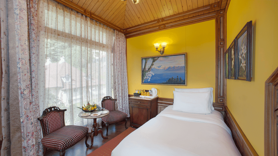 Standard guest room at MAYFAIR Hill Resort Darjeeling with a single bed, yellow wood-panelled walls, and a sitting nook by the window