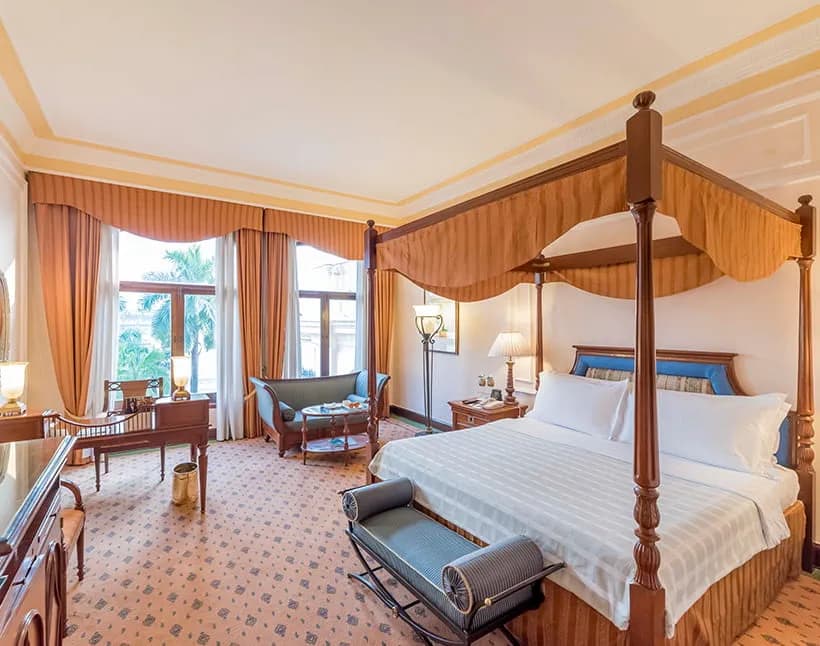 Premier Room at The Oberoi Grand, Kolkata, with a dark wood four-poster bed, striped drapery, and tall windows