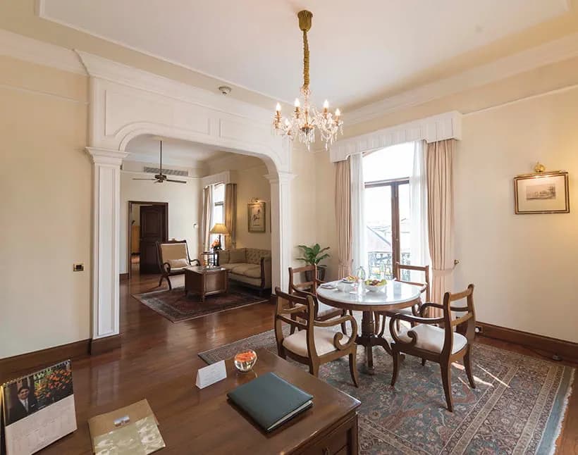 Luxury Suite living and dining area at The Oberoi Grand, Kolkata, with a round dining table, crystal chandelier, and a connecting sitting room
