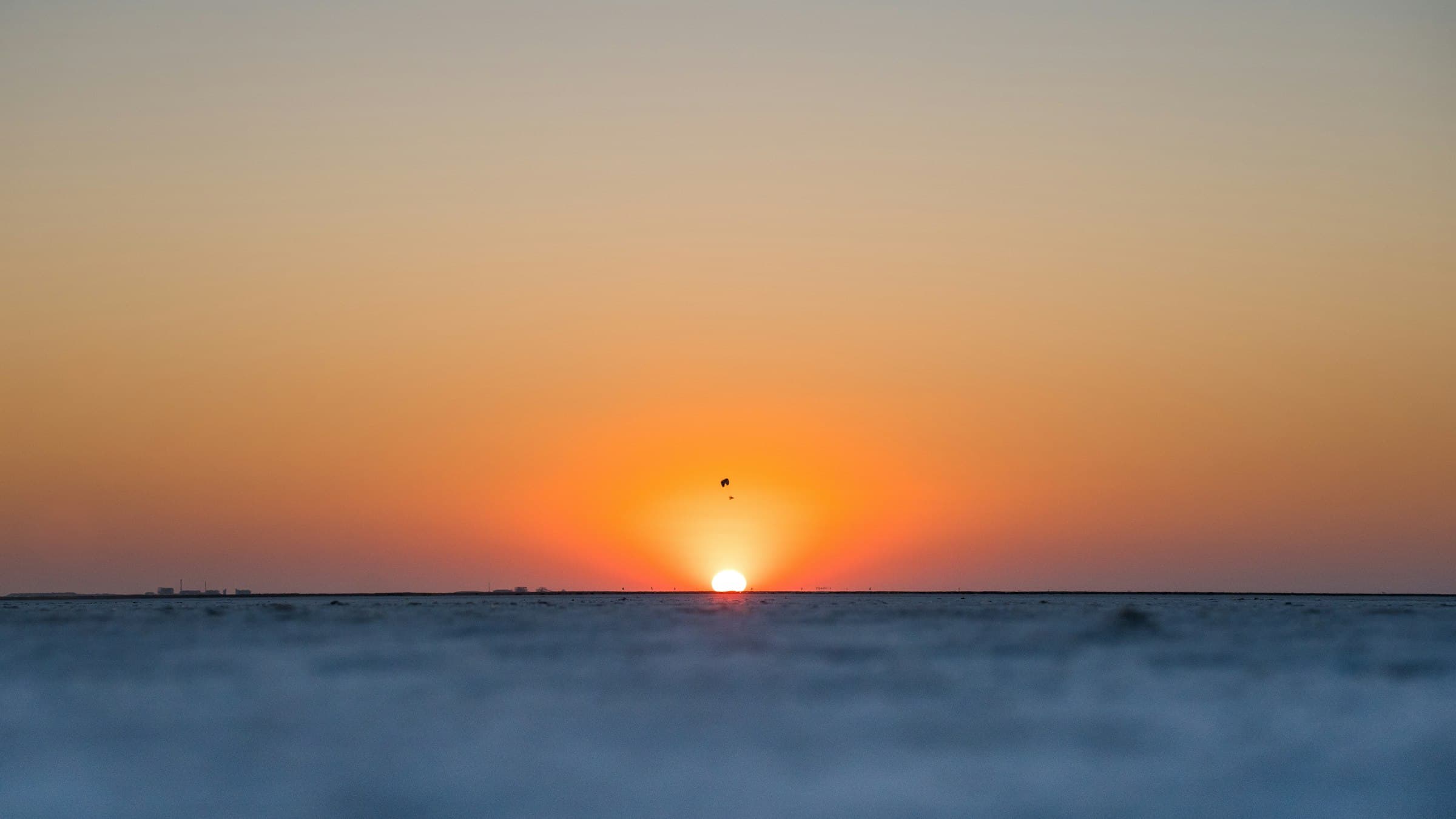 Sun setting on the flat horizon of the Great Rann of Kutch salt flats, Gujarat, with a few figures in silhouette