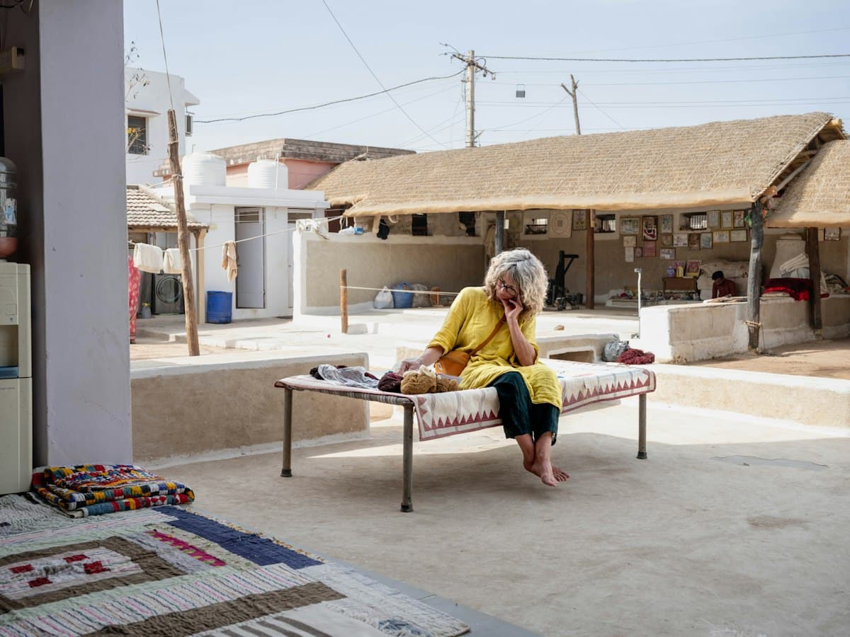 A woman sorting hand-spun yarn on a charpoy in a courtyard with thatched roofs at Bhujodi, Kutch, Gujarat
