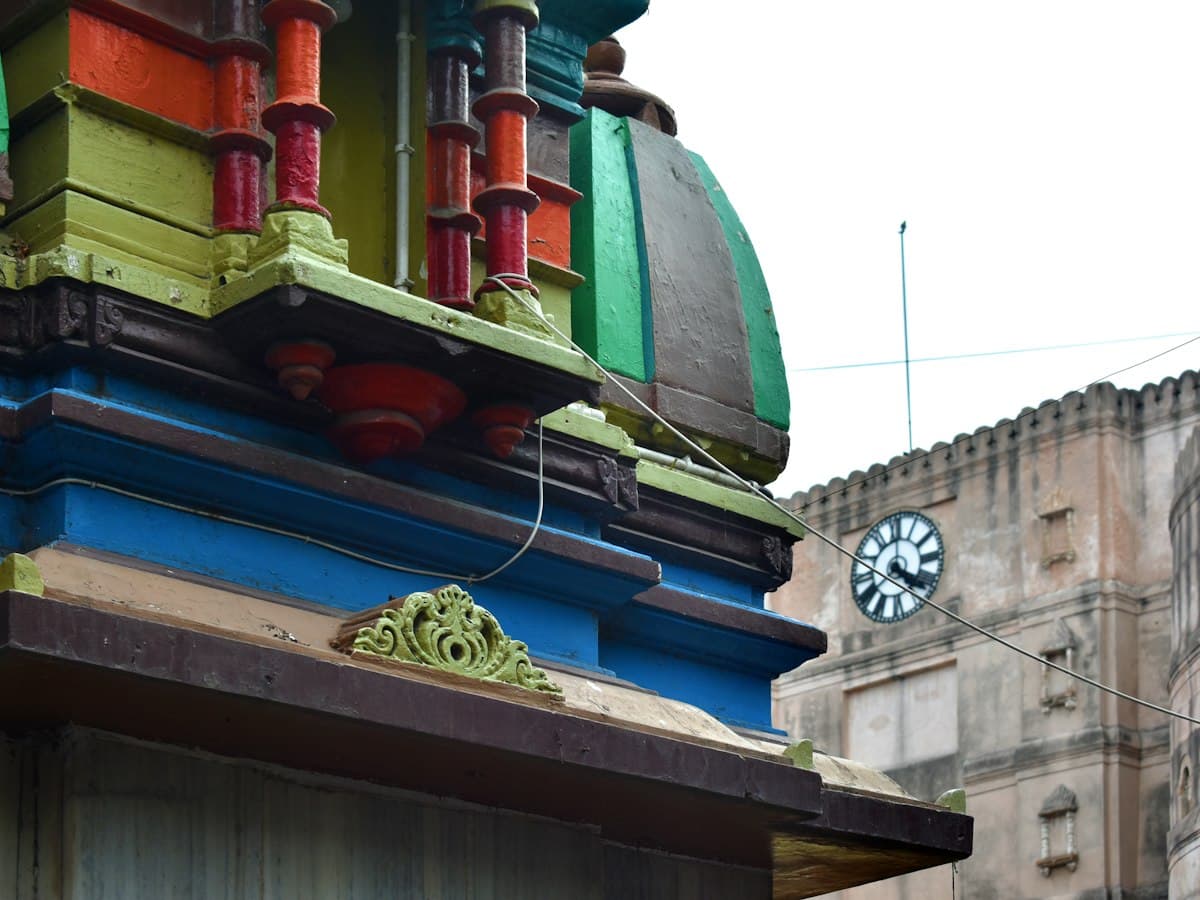 Painted temple spire beside a clock-fronted stone building near Bhadra Fort, Old City, Ahmedabad