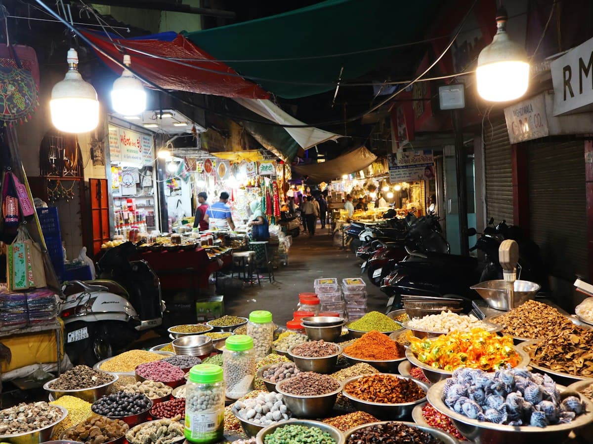 A night-time Ahmedabad market lane with bowls of dried fruit, nuts and sweets under bare bulbs