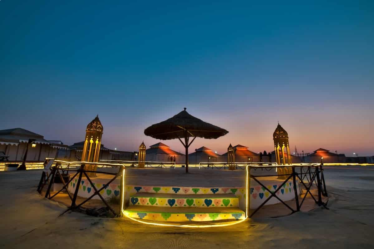 Dusk over Rann Utsav Tent City, Dhordo, with a parasol lounge deck and lanterns lit against a blue sky