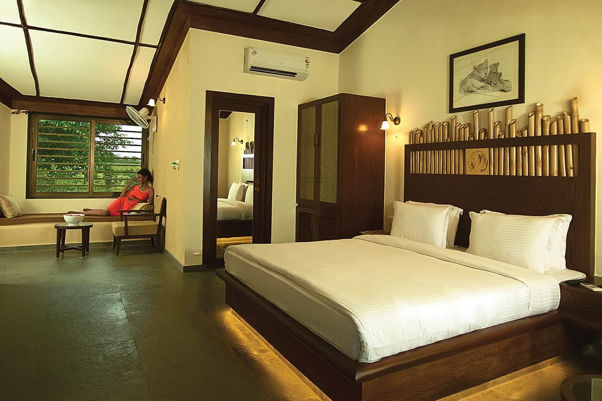 Deluxe AC Cottage bedroom with king bed and bamboo-detail headboard at Asiatic Lion Lodge