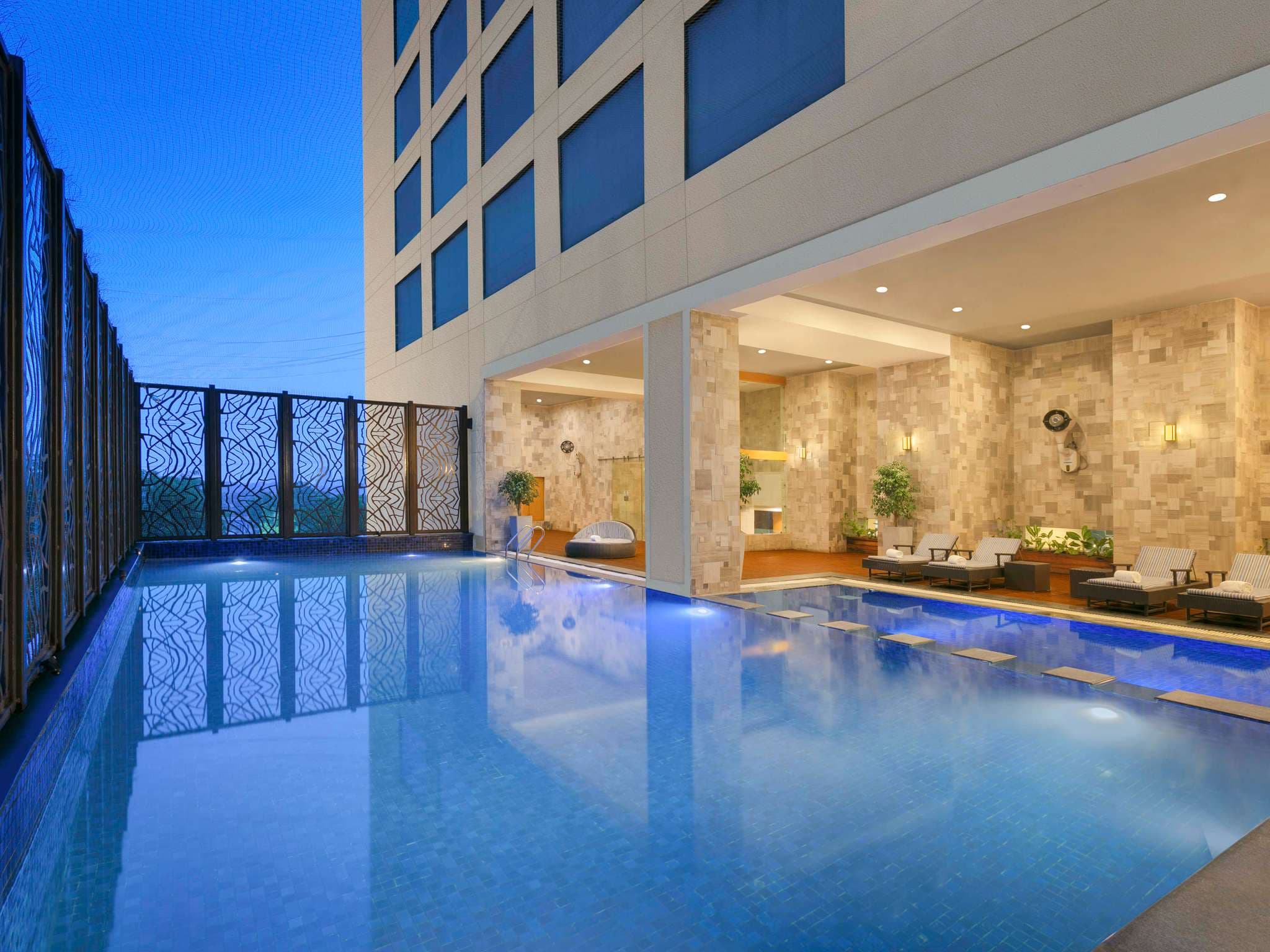 Open-air swimming pool with stone-clad cabanas at Novotel Ahmedabad