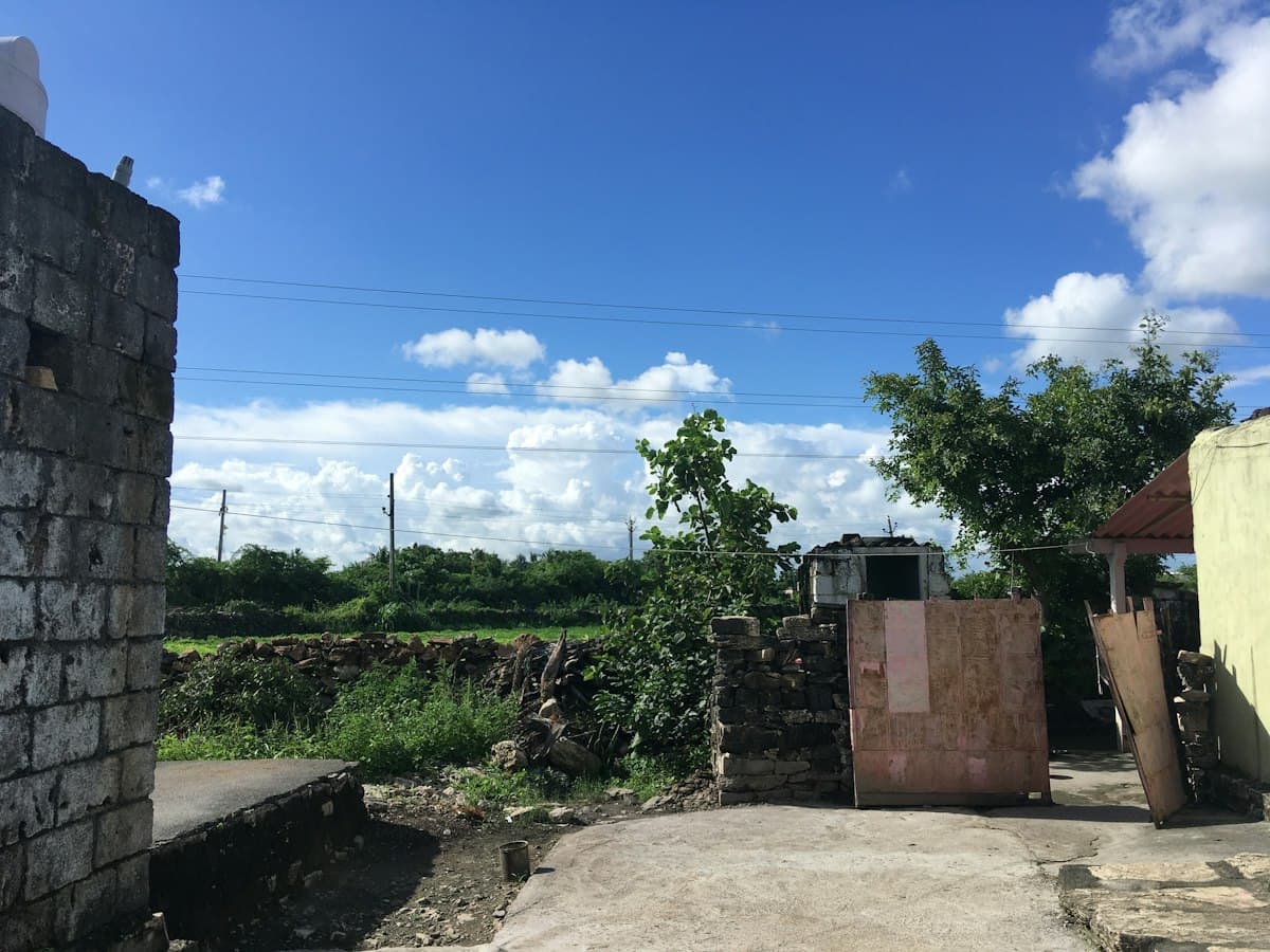 Green fields and village rooftops under a blue sky with clouds near Sutrapada in the Gir Somnath countryside, Saurashtra, Gujarat