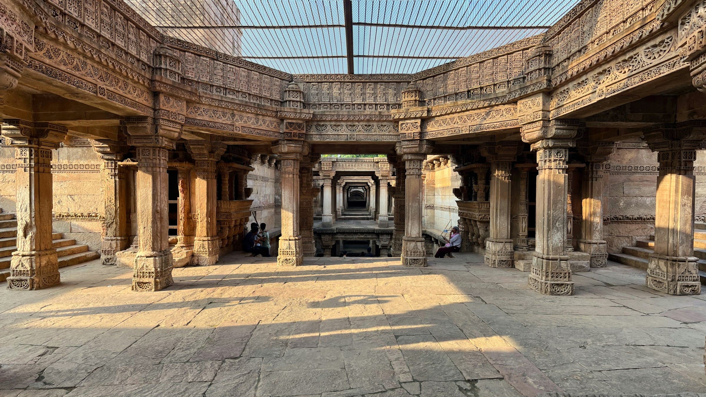 Carved sandstone pillars and galleries inside Adalaj Stepwell near Ahmedabad, Gujarat, with light falling across the floor