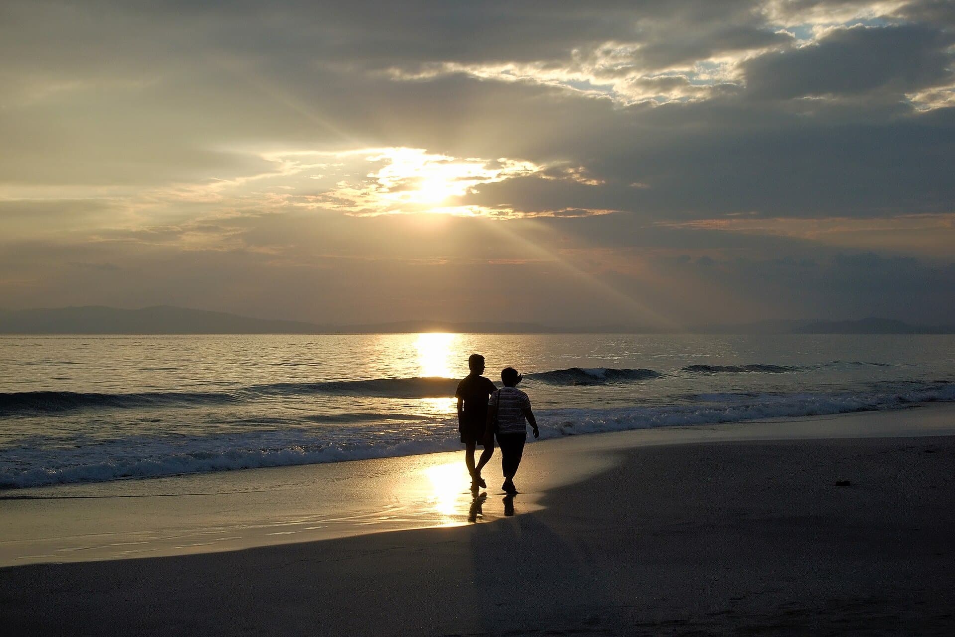 A couple walking along the waterline as the sun sets over the sea on Havelock Island, Andaman Islands