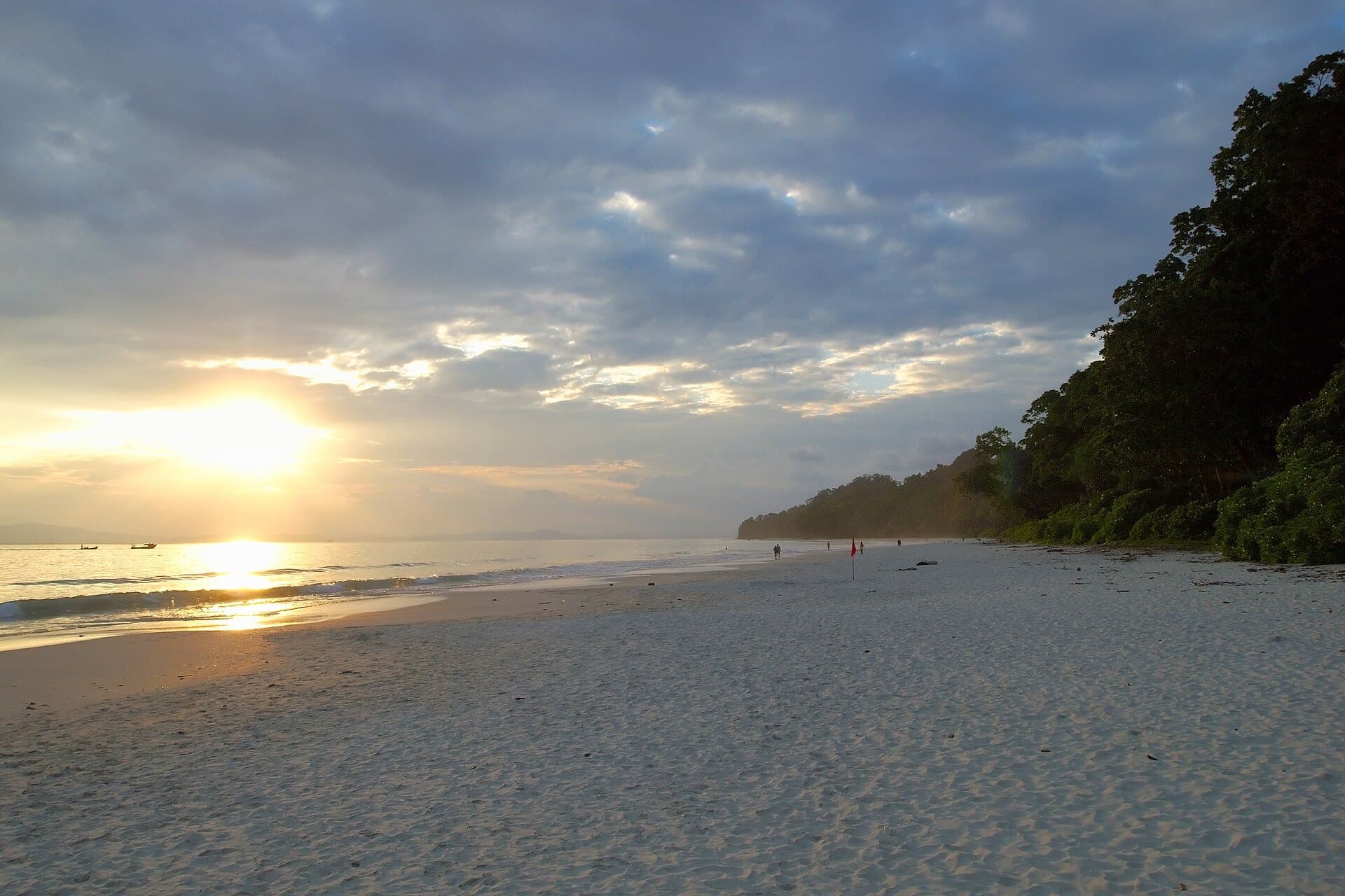 Low golden sun over calm water and pale sand with a forested headland, Radhanagar Beach, Havelock Island