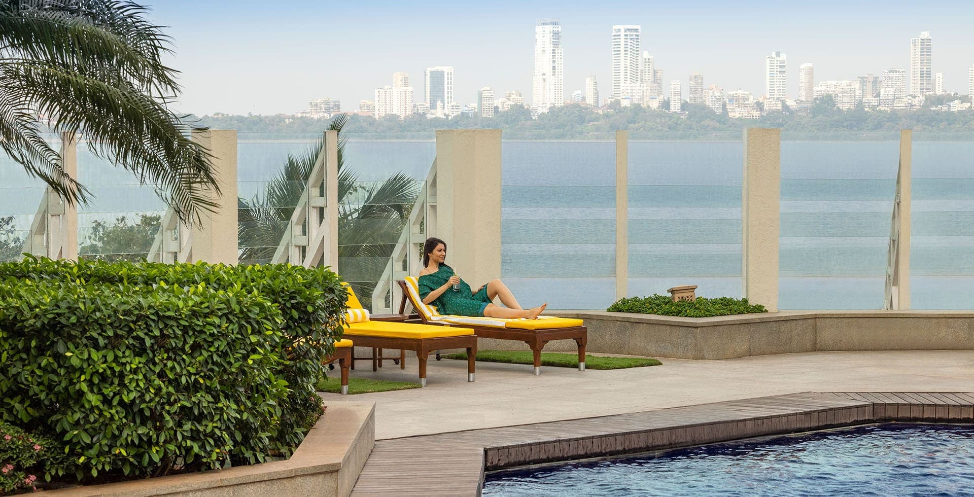 Pool terrace with sun loungers and a glass balustrade facing the Mumbai skyline at The Oberoi, Mumbai