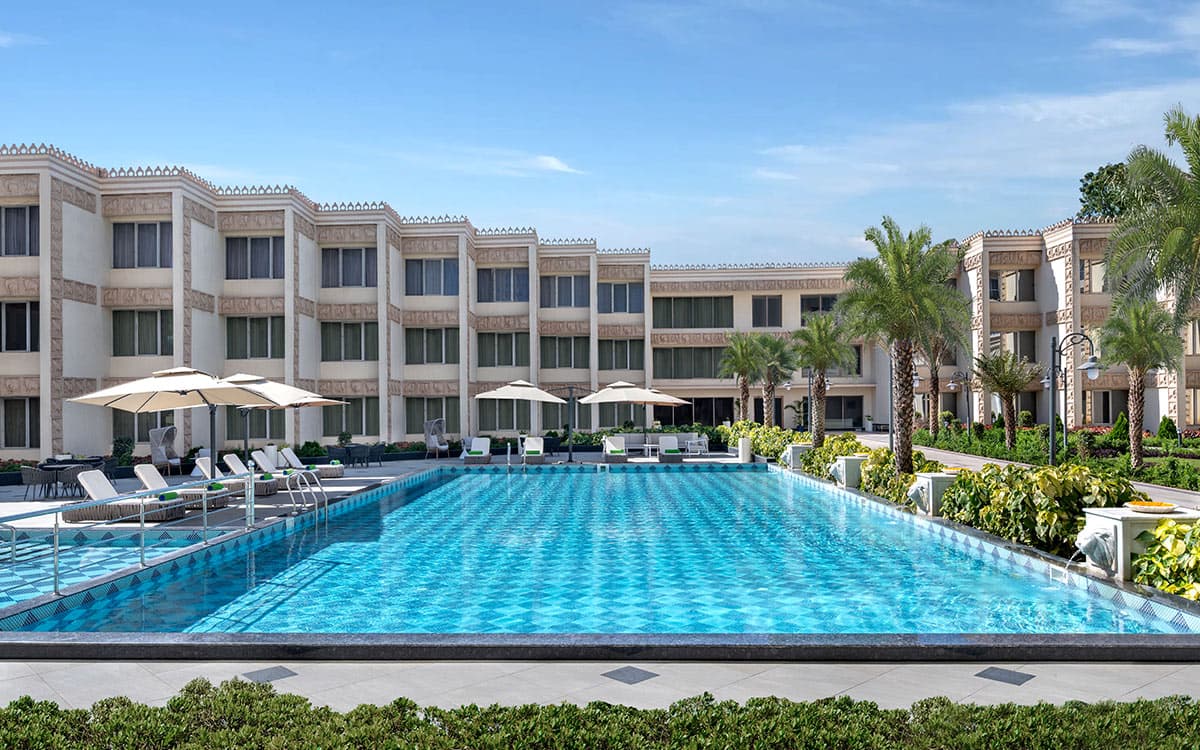 Outdoor pool with parasols and the arched hotel wing at Welcomhotel Rama International, Aurangabad