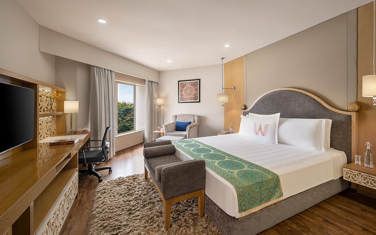 Deluxe Suite bedroom with a king bed, carved wooden screen and armchair at Welcomhotel Rama International