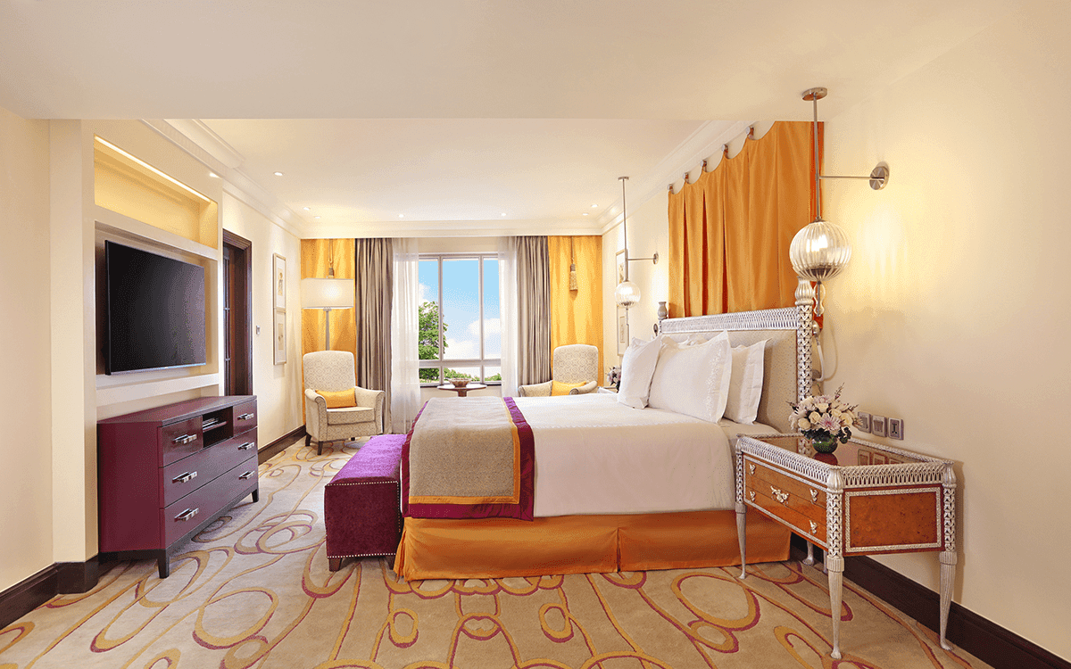 Luxury Suite bedroom with a king bed, bench and warm gold drapes at ITC Maratha, Mumbai