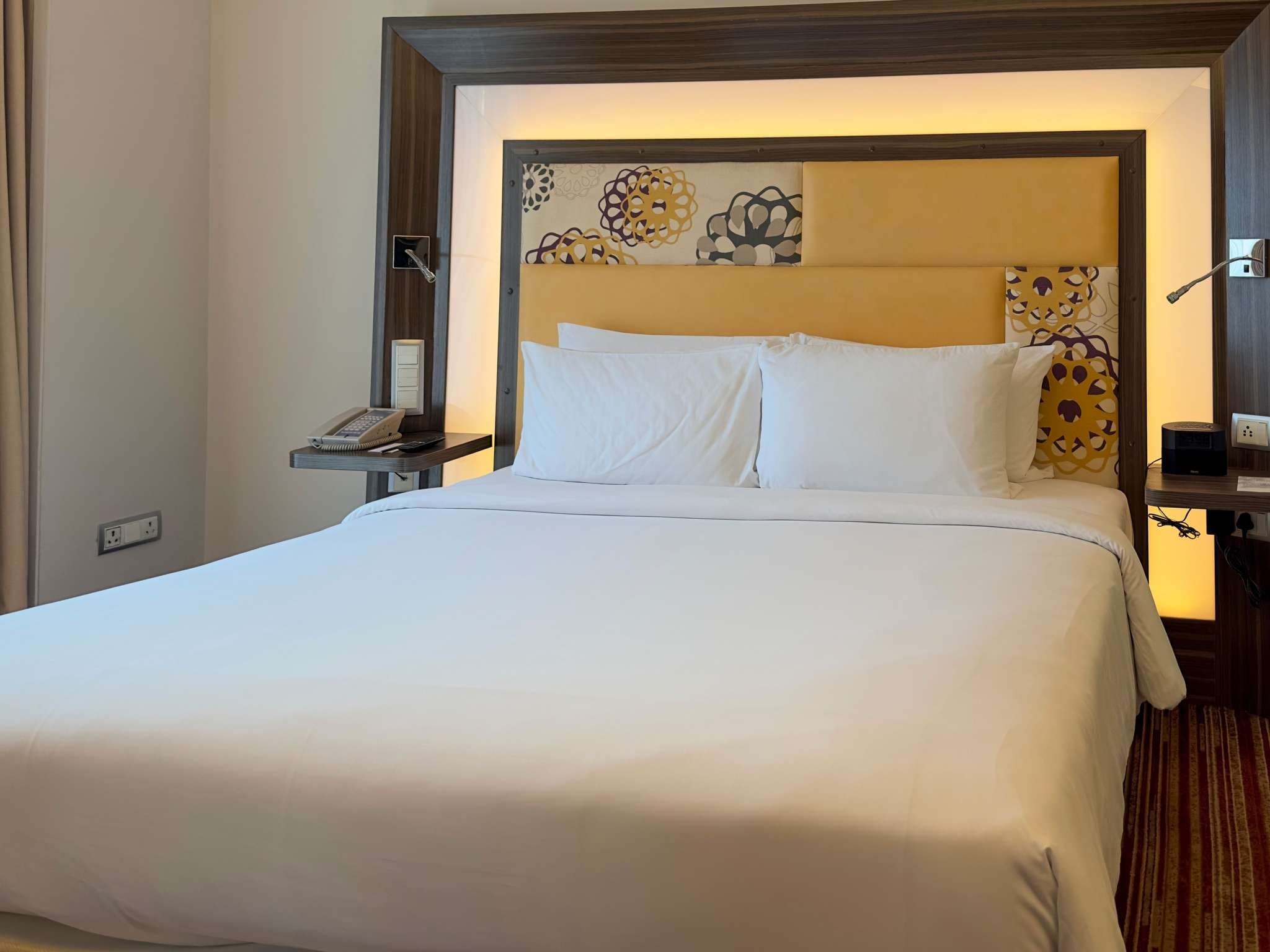 Deluxe King room bed with a gold backlit headboard at Novotel Pune Nagar Road
