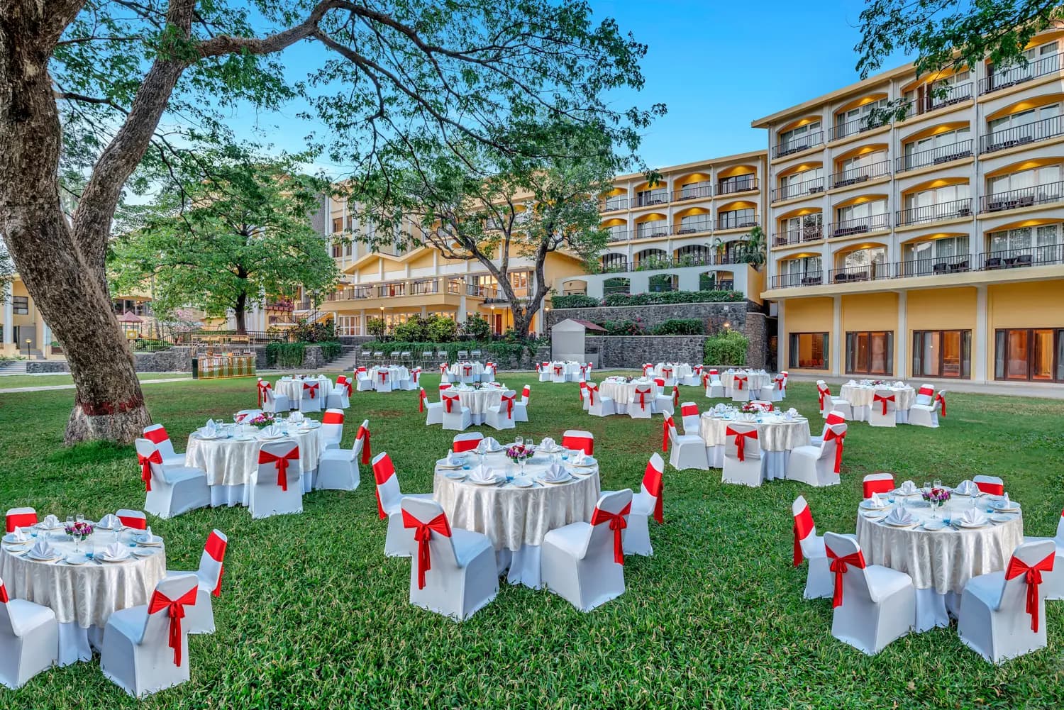 Resort wing and lawn set for a gala dinner under a large tree at Fariyas Resort Lonavala