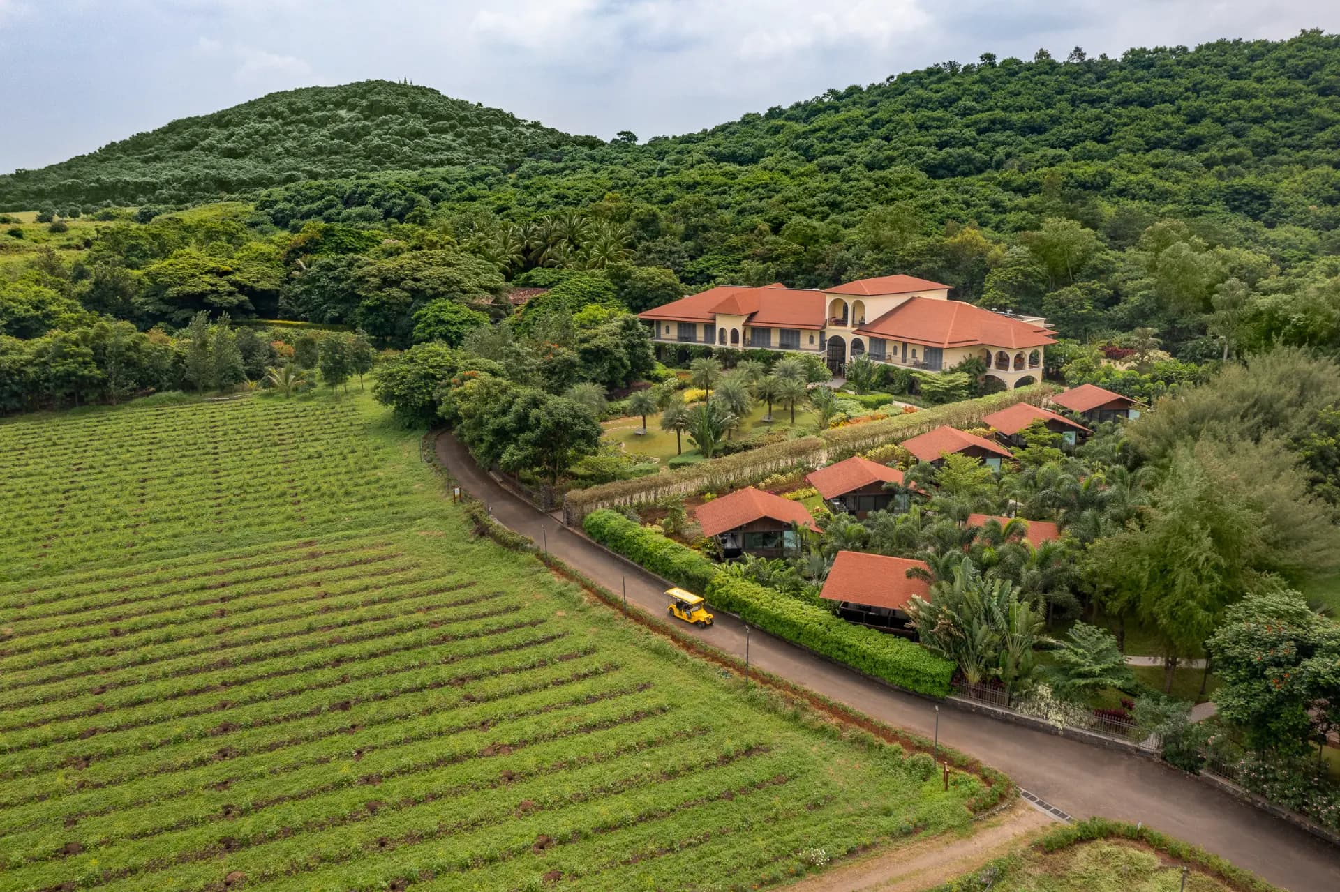 Aerial view of terracotta-roofed villas and vine rows below green hills at The Source at Sula, Nashik